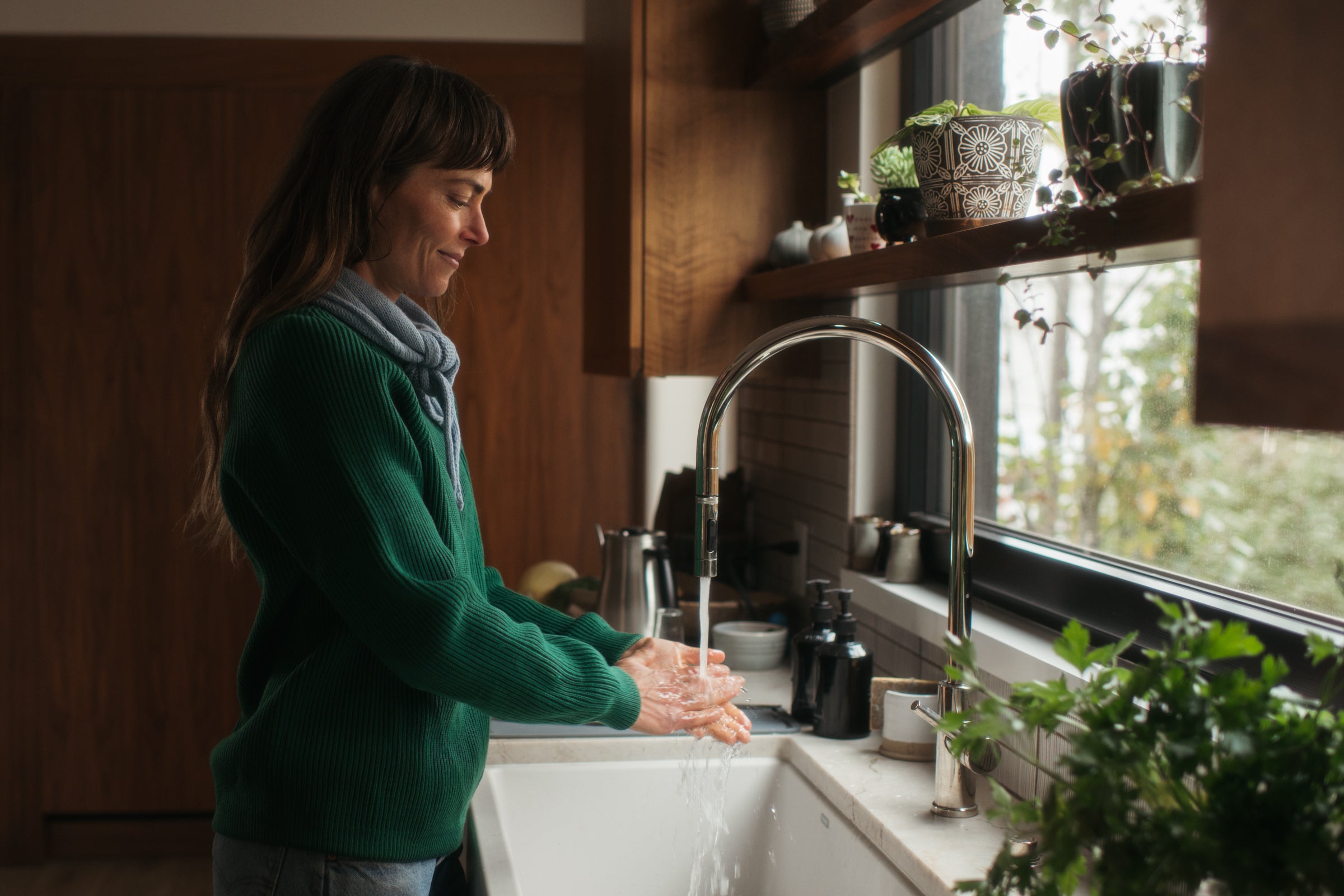 Woman washing hands in a kitchen sink with a window in the background